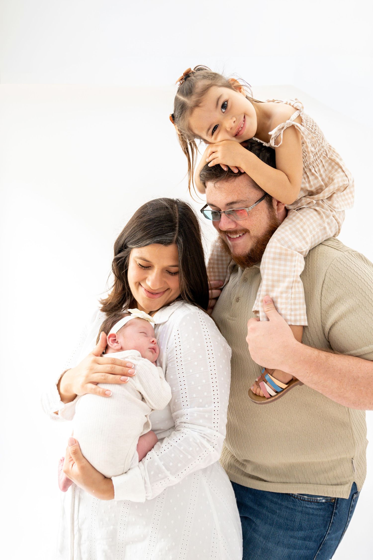 Family portrait with newborn baby in white against bright background.