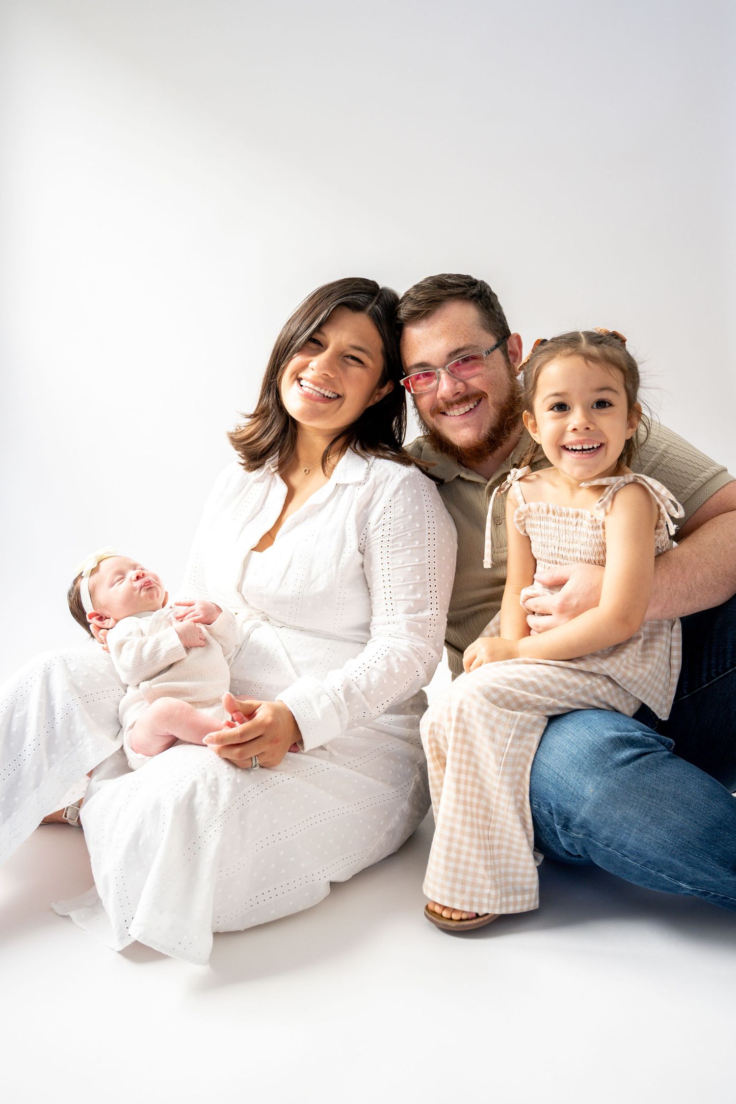 Family lounging together on white floor with newborn baby.