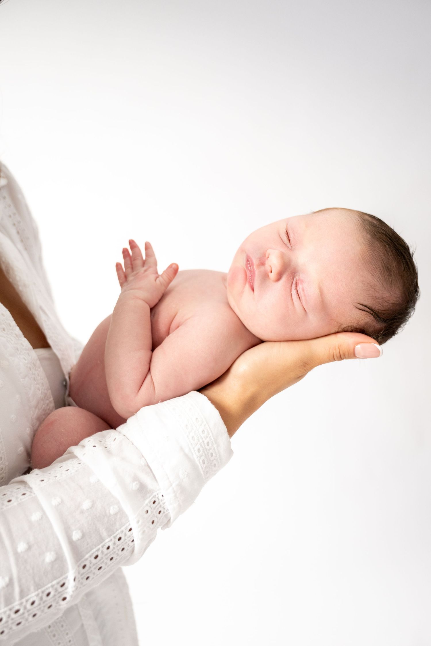Sleeping newborn baby in white swaddle against light background.