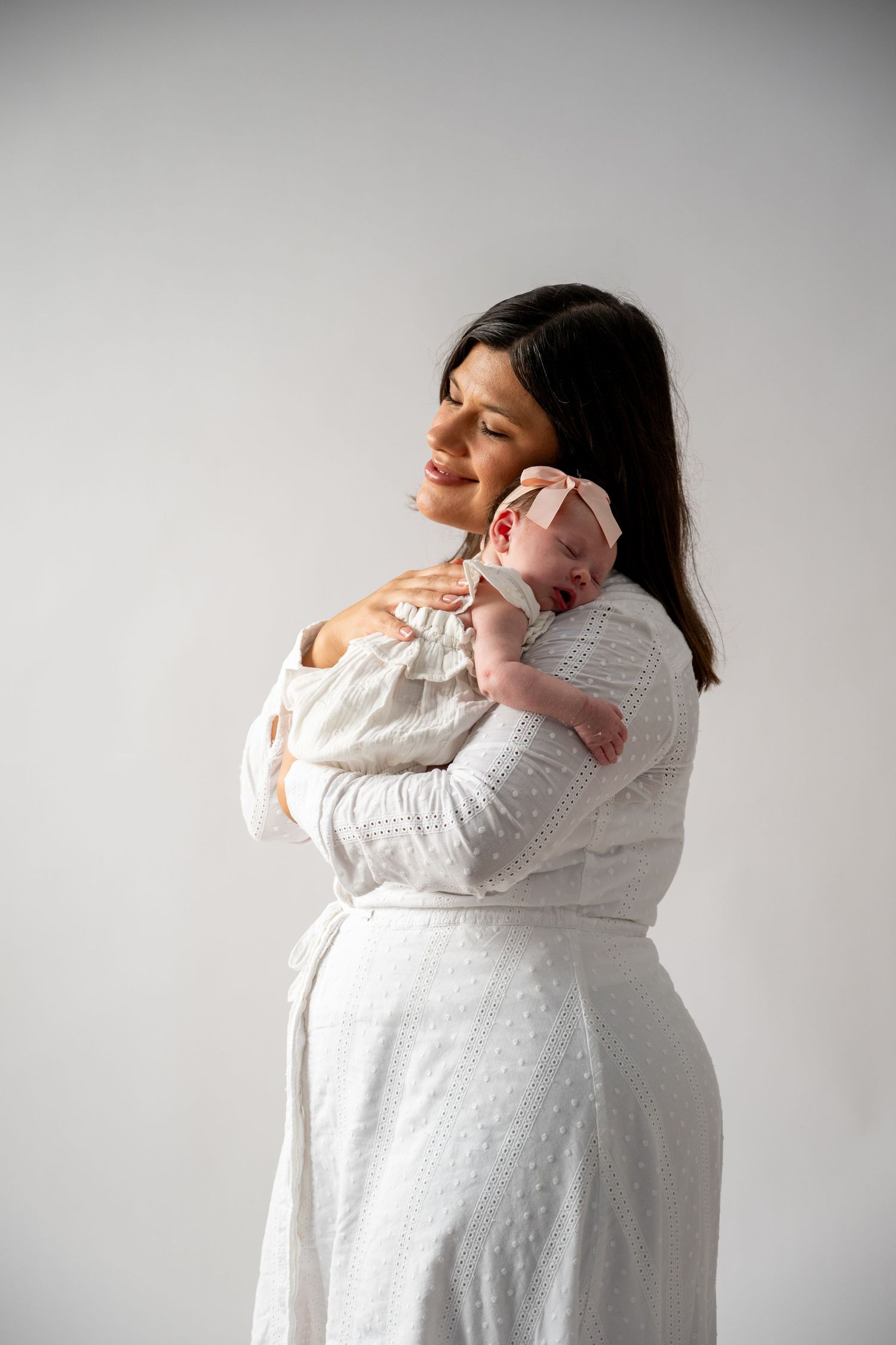 Woman in white dress holding and comforting newborn baby.