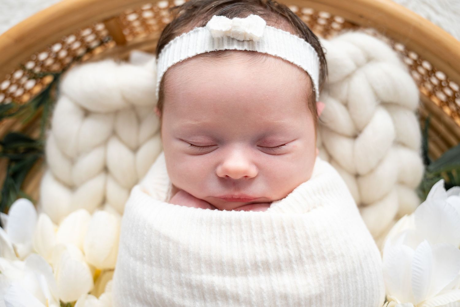 Peaceful sleeping newborn baby in white knit wrap on cream textured basket.