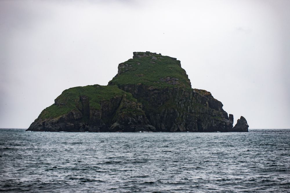 Isolated rocky island with green vegetation rises from the misty ocean waters.