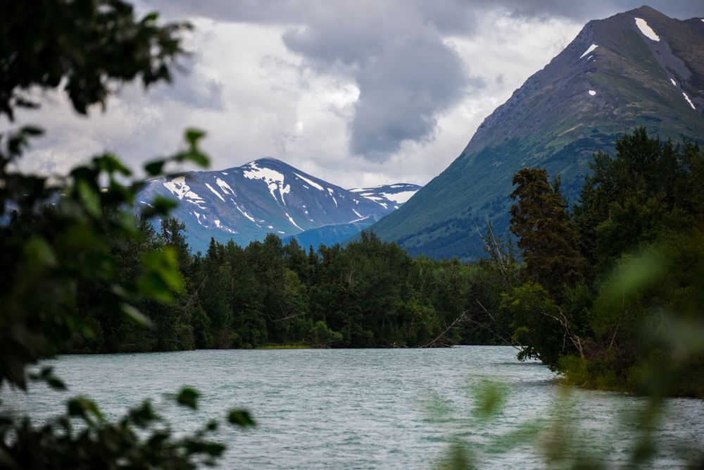 Snow-capped mountains tower over a serene lake surrounded by lush forest.