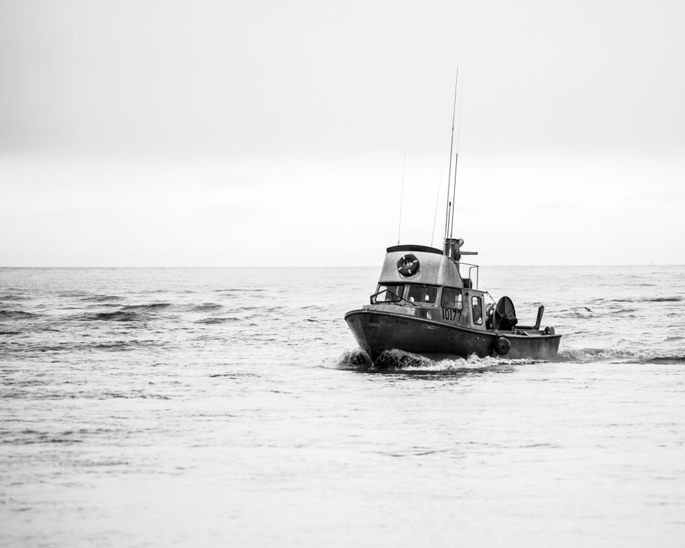 A small fishing boat navigates rough waters in black and white.