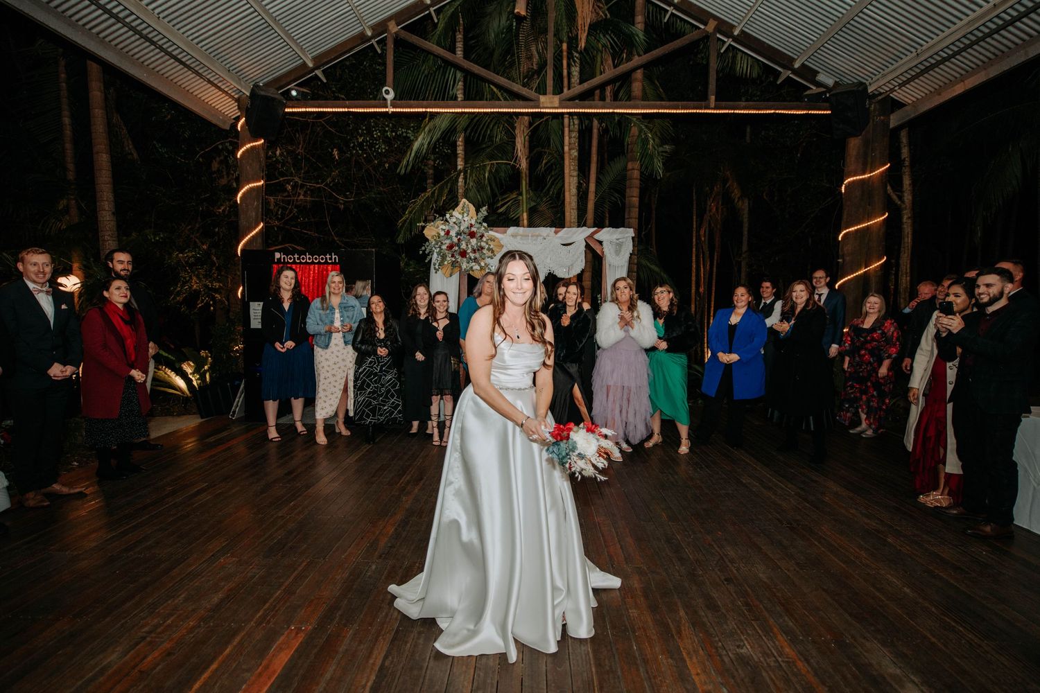 Bride prepares to toss bouquet during wedding reception in rustic wooden venue.