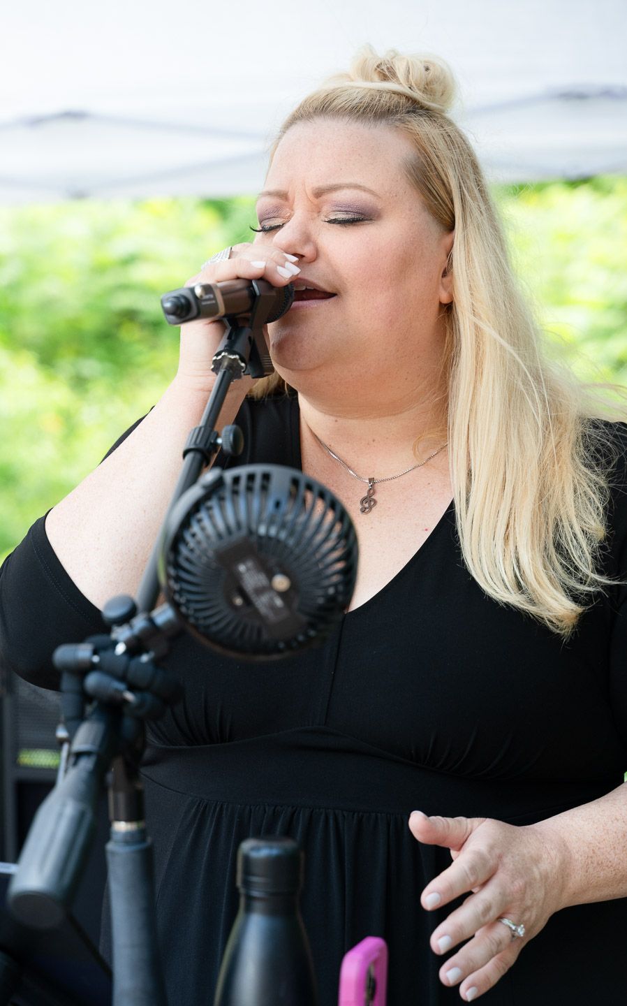 Pixs By Tina captures a woman performing in a black dress singing passionately into a microphone during an outdoor performance.