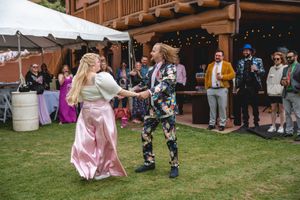 A couple dances together on grass at an outdoor wedding reception with string lights and guests watching.