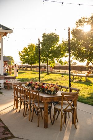 Elegant outdoor wedding reception table with wooden chairs and floral centerpieces at sunset.