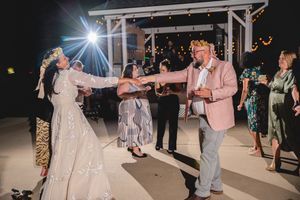 Wedding party dancing outdoors under a white gazebo at night with dramatic lighting.