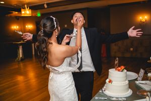 Playful moment as couple smears wedding cake on each other's faces during reception.