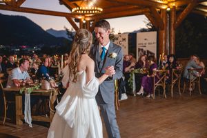 Couple shares their first dance at sunset during outdoor mountain reception under rustic wooden pavilion.