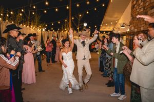 Bride and groom in cowboy hats celebrate grand exit under string lights at rustic outdoor wedding reception.