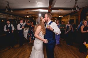 Newlyweds dancing together on a wooden dance floor under dim lighting at their reception.