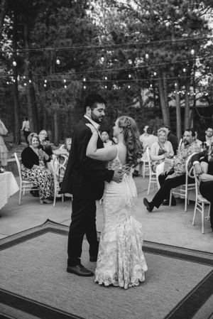 Romantic first dance on outdoor patio with string lights and guests watching.