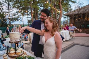 Couple cutting their wedding cake outdoors at sunset with string lights in the background.