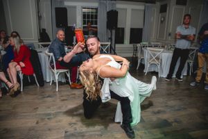 Dramatic dip dance move during wedding reception on rustic wooden floor.