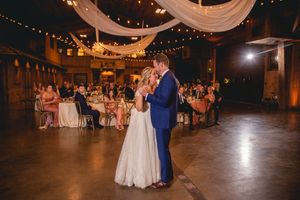 A couple shares their first dance in a rustic venue decorated with string lights and white drapery.