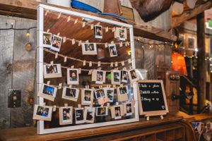 Rustic wedding photo display with polaroid pictures hung on string lights against wooden backdrop.