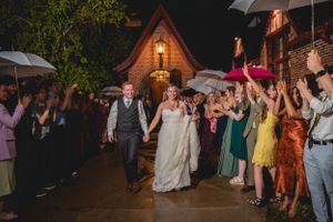 Wedding party exit at night with guests holding umbrellas and sparklers outside Tudor-style venue.