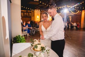 A couple cutting their white wedding cake together during their reception celebration.