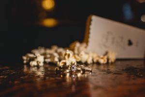 Wedding rings and jewelry details captured in artistic macro photography on a dark wooden surface.