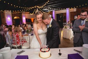 Couple cutting their small wedding cake under string lights at reception venue.