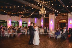 Wedding reception ballroom with string lights, chandelier and couples dancing.