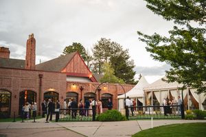 Guests mingle outside a charming brick Tudor-style venue with a white tent during an outdoor evening event.