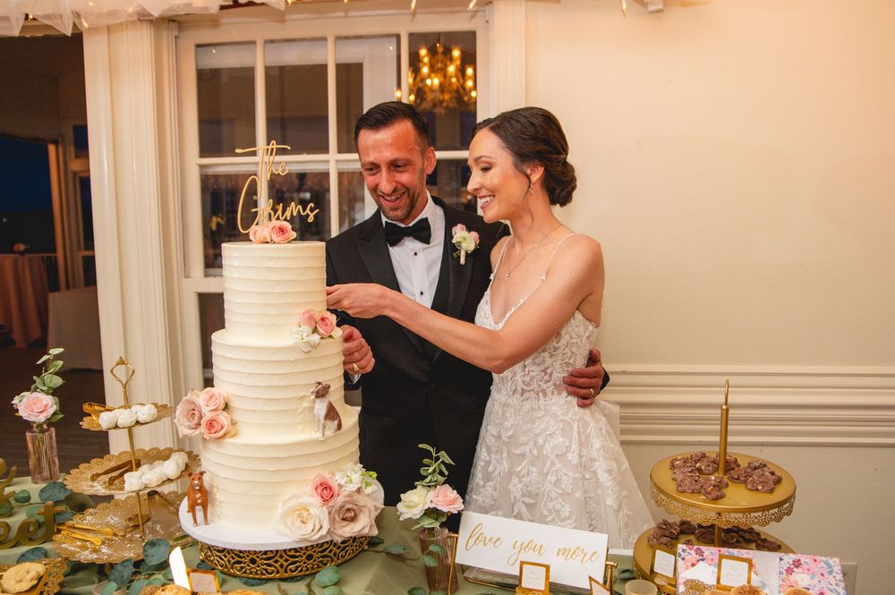 A couple cuts into a four-tier white wedding cake decorated with fresh flowers at an elegant reception.