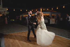 A couple dances on an outdoor dance floor under string lights at their wedding reception.