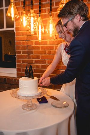 A couple cuts their simple white wedding cake under vintage Edison bulb lighting.
