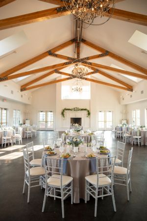 A bright reception venue with exposed wooden beams, chandeliers, and elegant table settings.