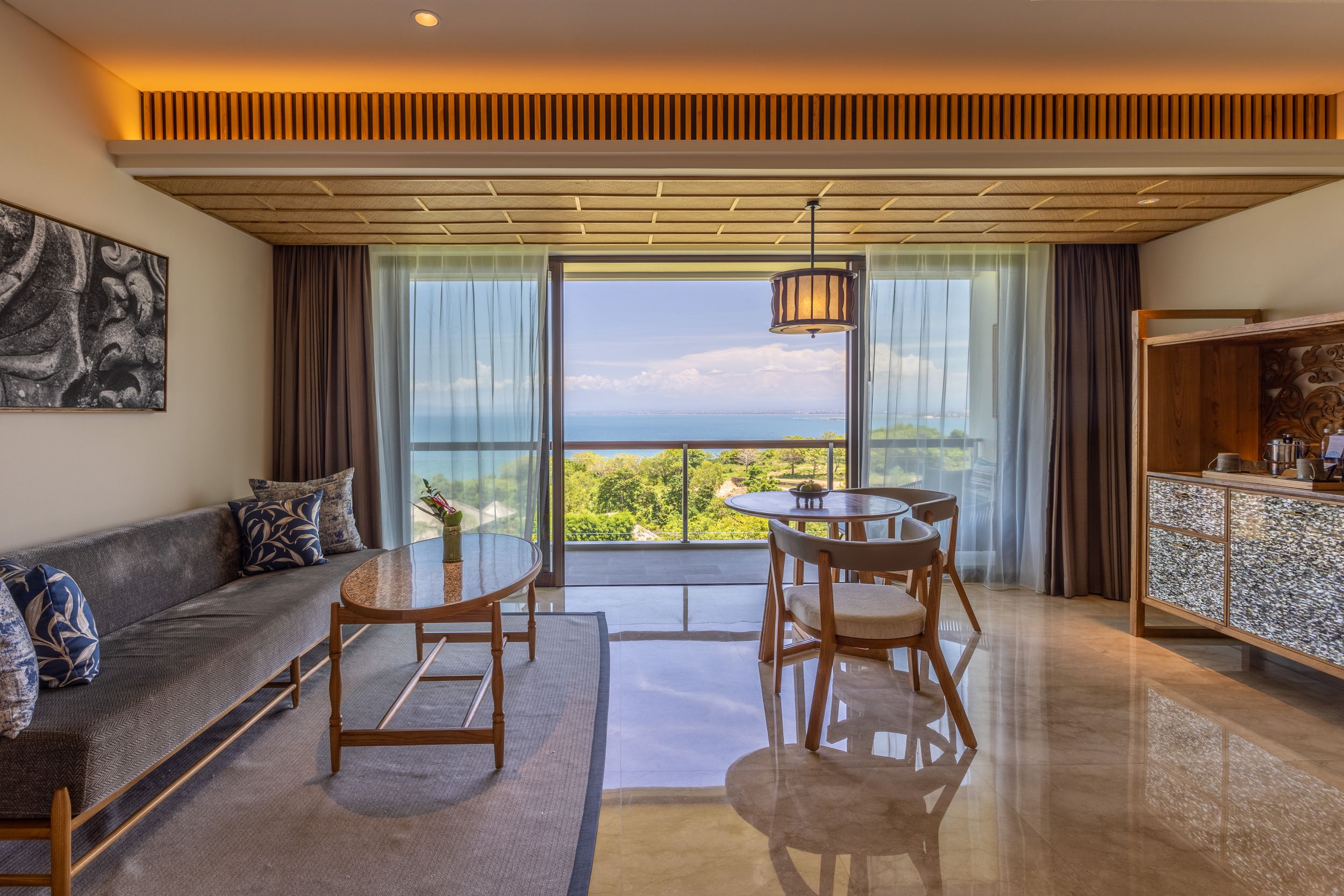 Spacious oceanfront hotel suite with modern furniture and panoramic sea views through floor-to-ceiling windows.