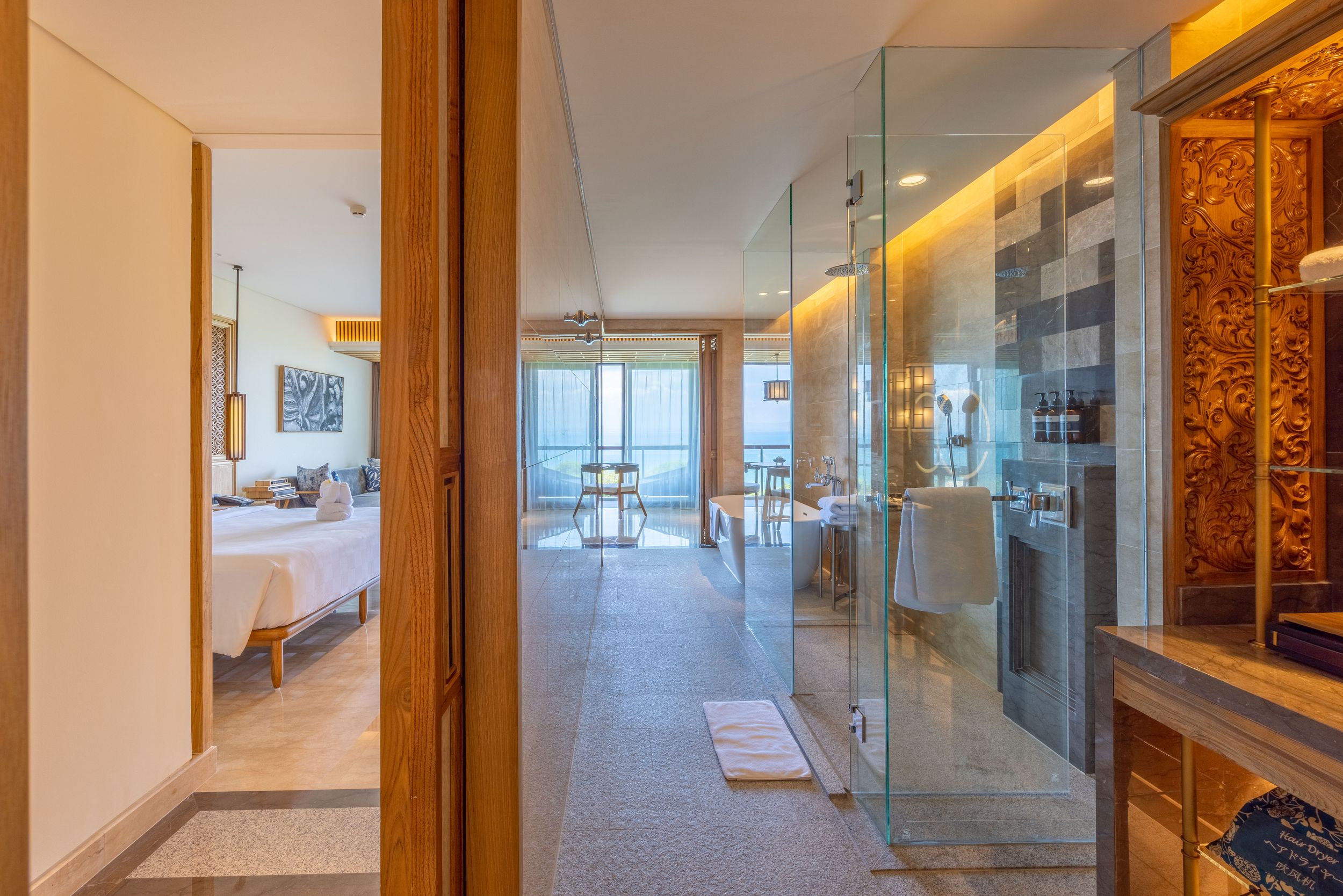 Elegant hotel suite entrance with glass doors and ocean view visible through corridor.