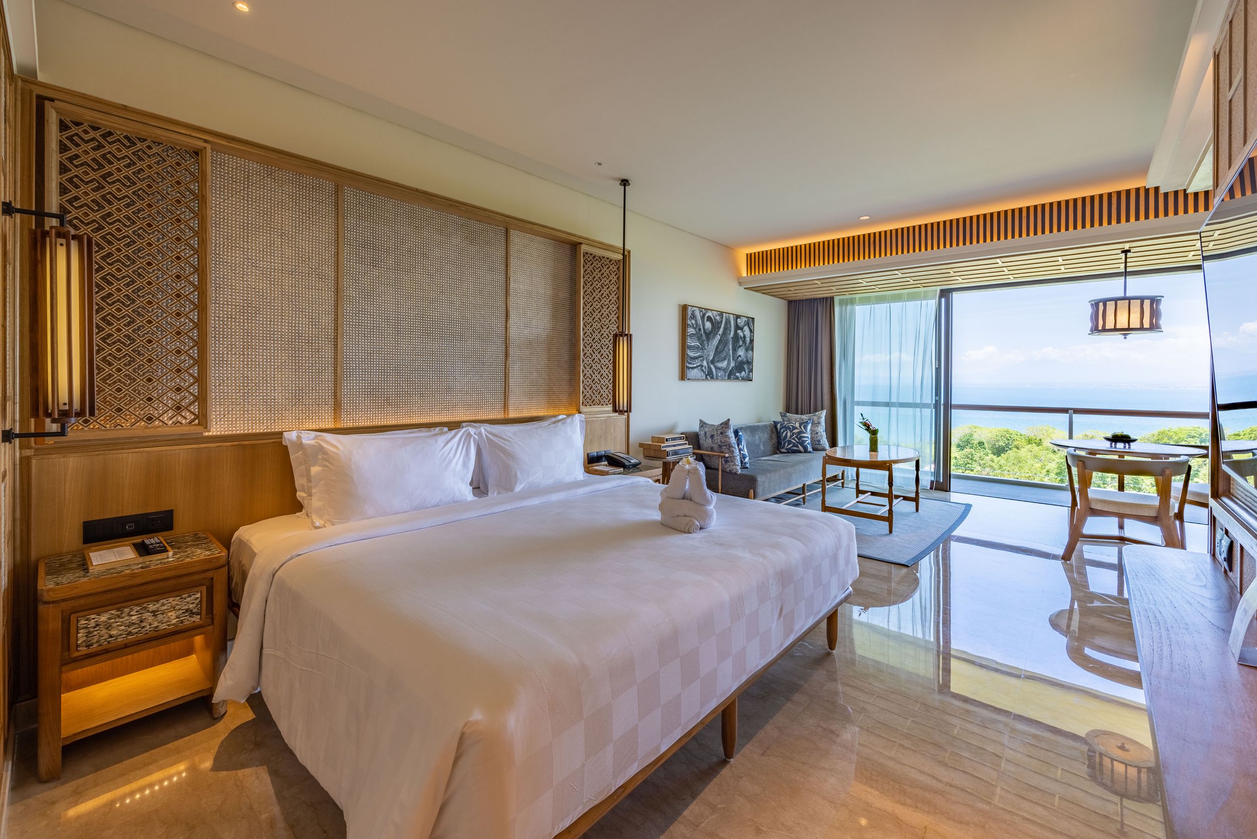 Luxurious hotel bedroom with king bed and ocean views through large windows.