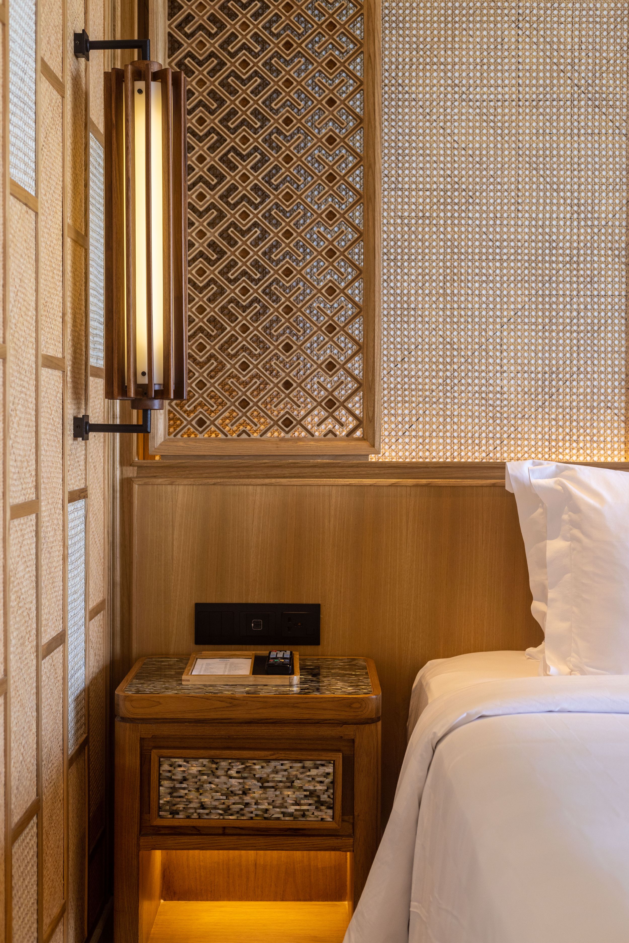 Luxurious hotel room bedside with geometric pattern screen and wall-mounted sconce light.