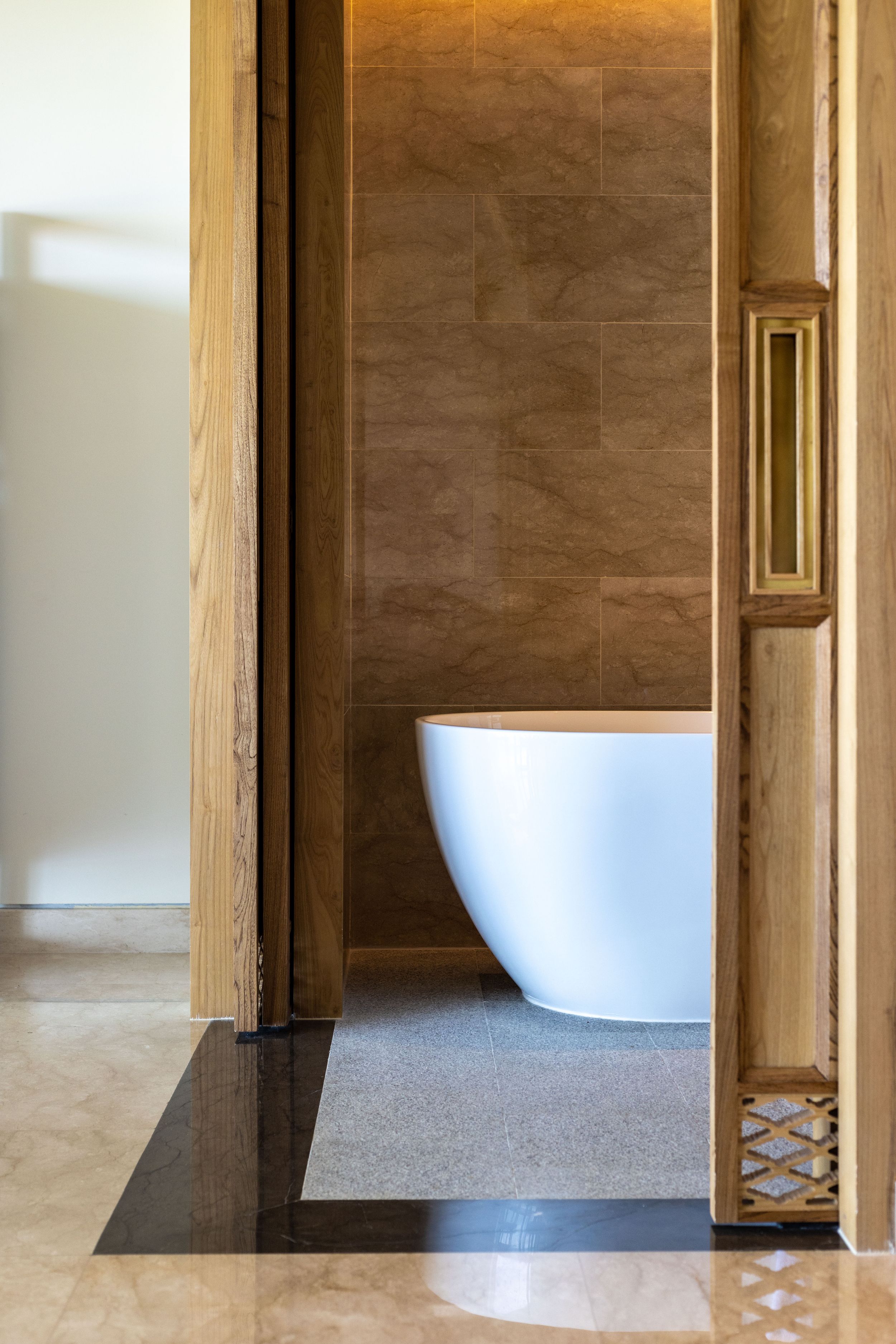 Modern bathroom entrance featuring a freestanding white bathtub and wooden door frame with decorative detail.