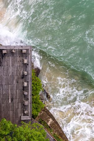 Aerial view of wooden deck overlooking dramatic ocean waves crashing against rocky shore.