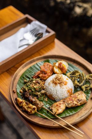 Traditional Indonesian rice dish served with grilled meats and vegetables on a banana leaf.