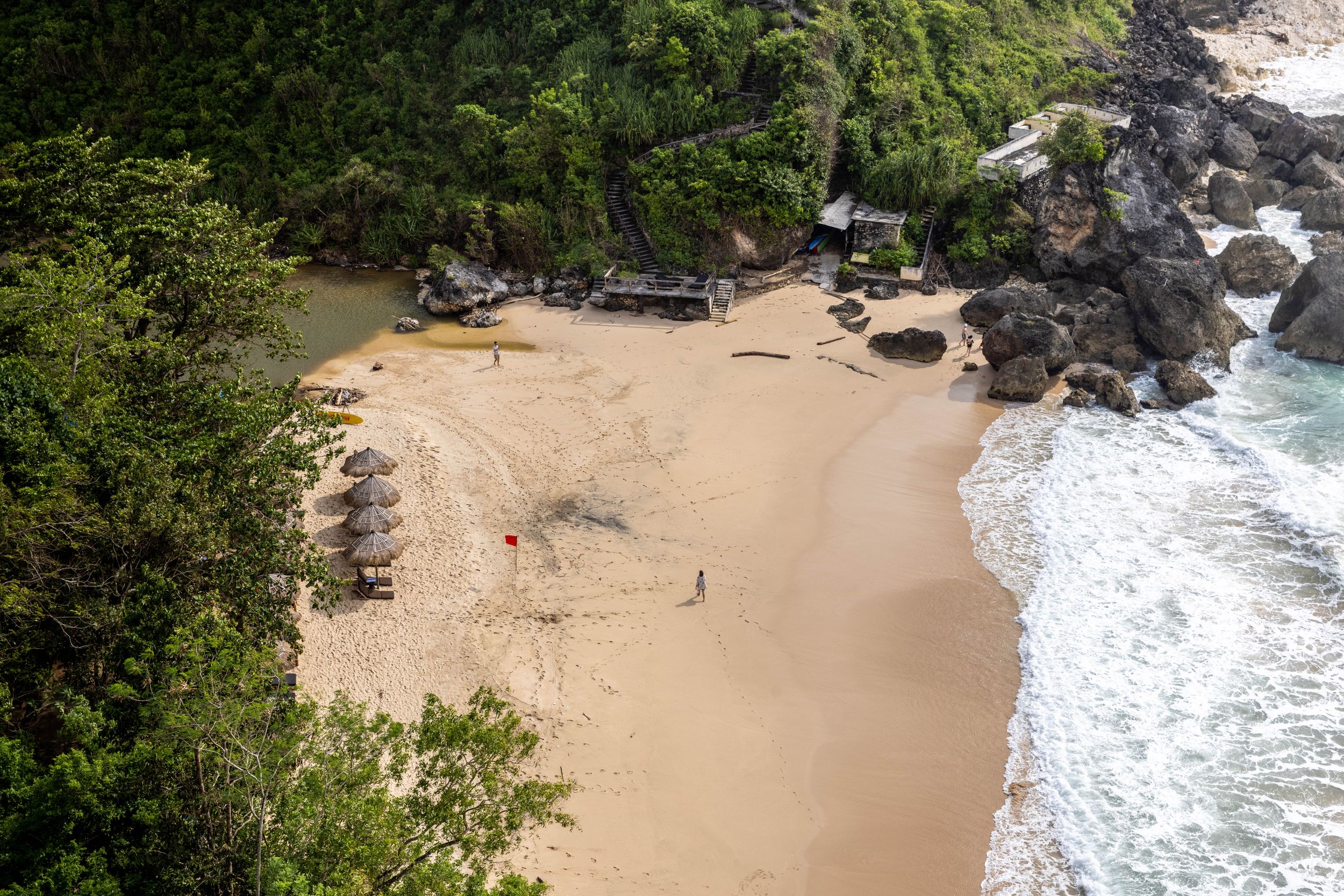 Aerial view of a secluded beach cove with black rocks and turquoise waters.