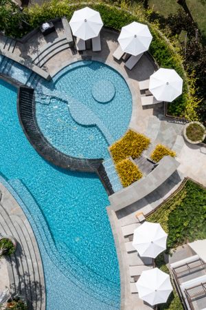 Overhead view of a curved swimming pool with white umbrellas and lounge chairs.