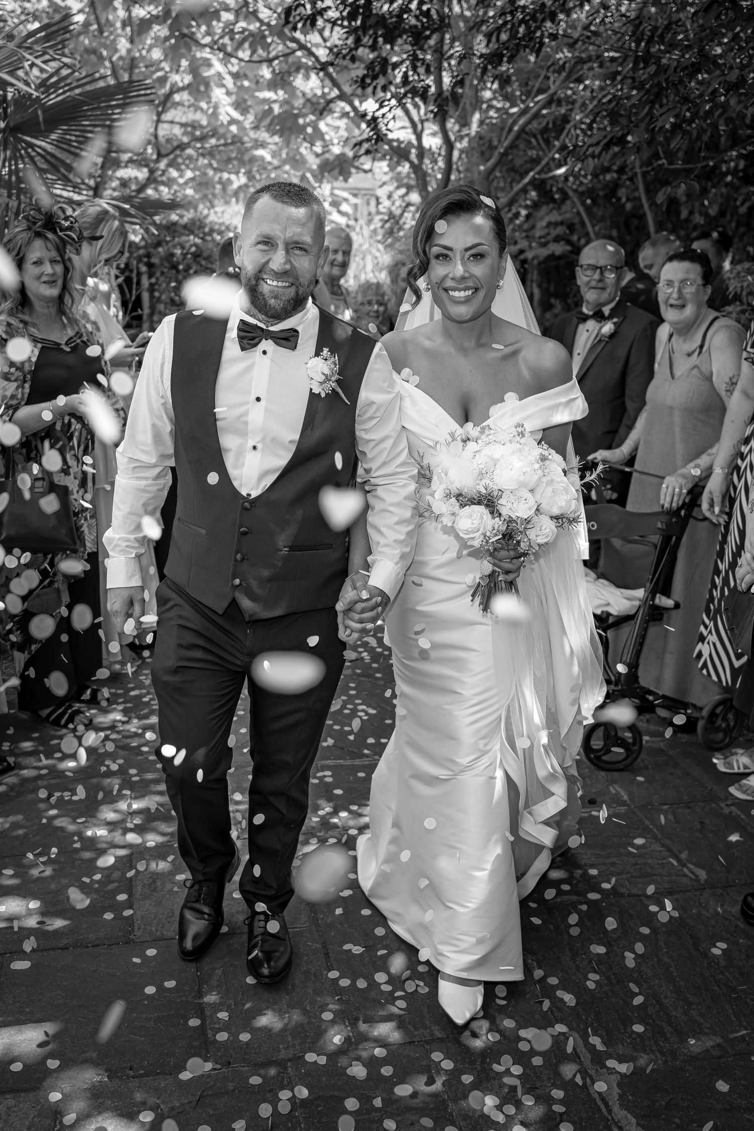 Black and white wedding celebration with guests showering the couple with confetti in a garden setting.