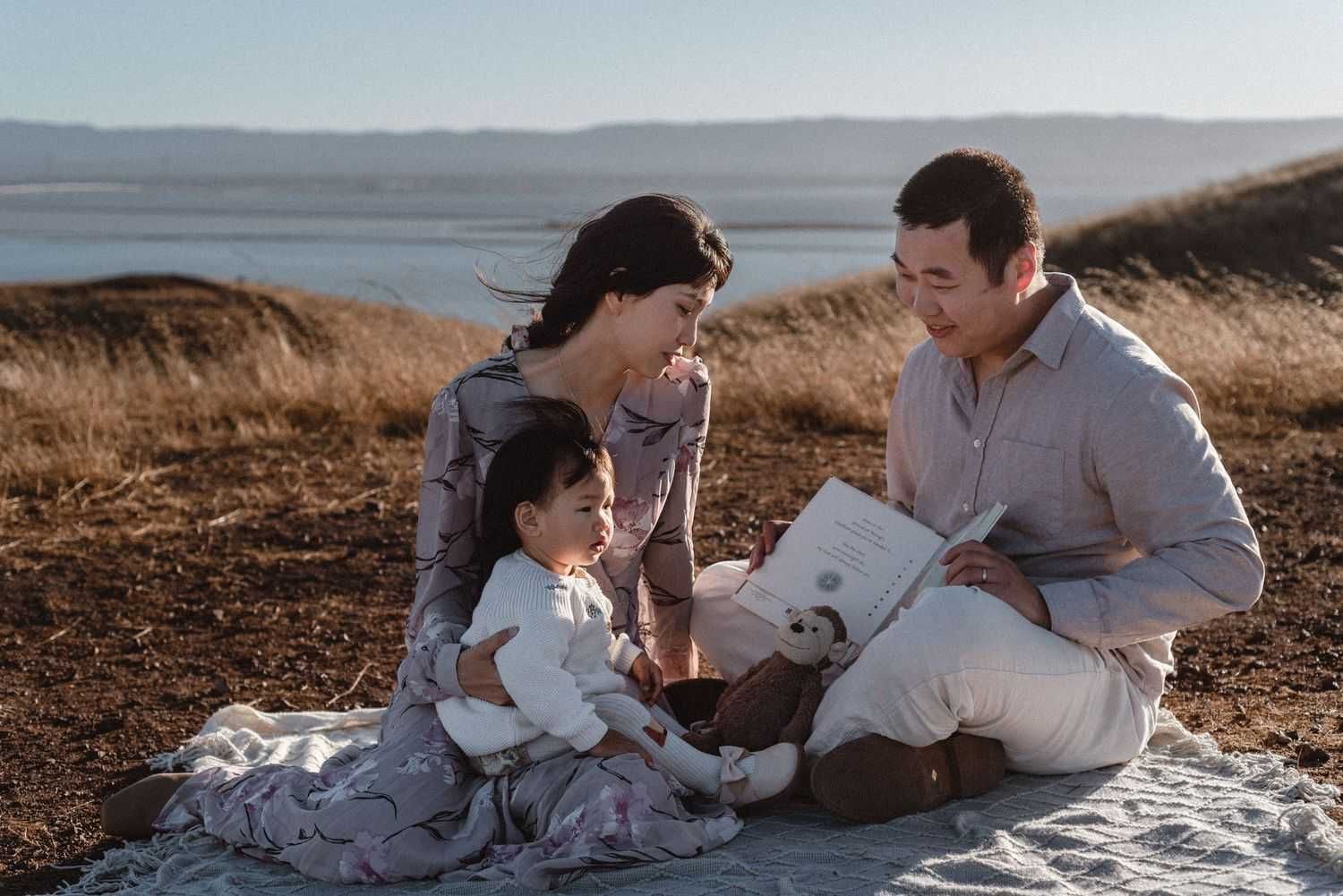 Family picnic scene on a blanket against scenic coastal hills.