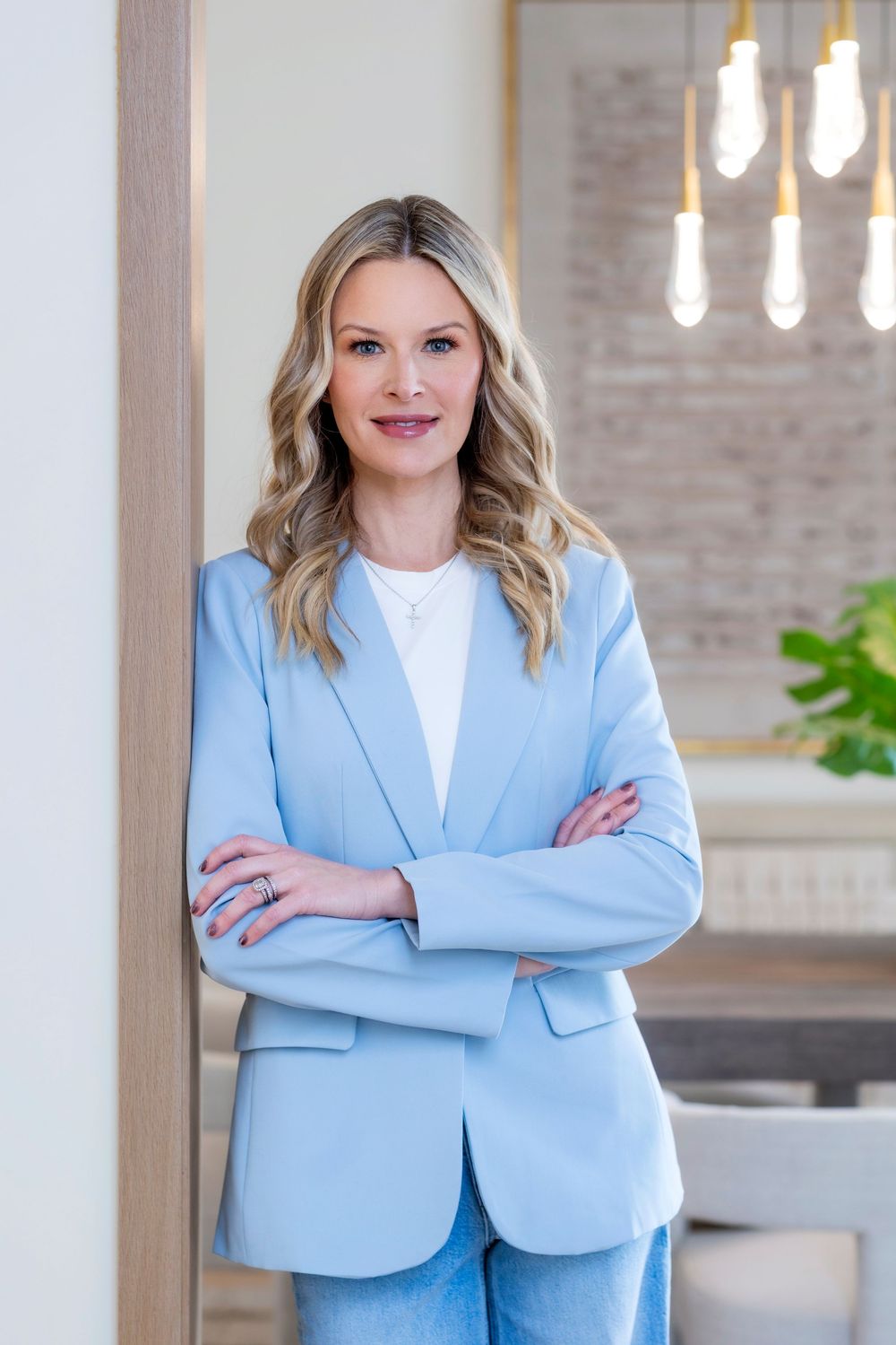 Professional wearing a light blue blazer and white top poses confidently in a modern office setting.