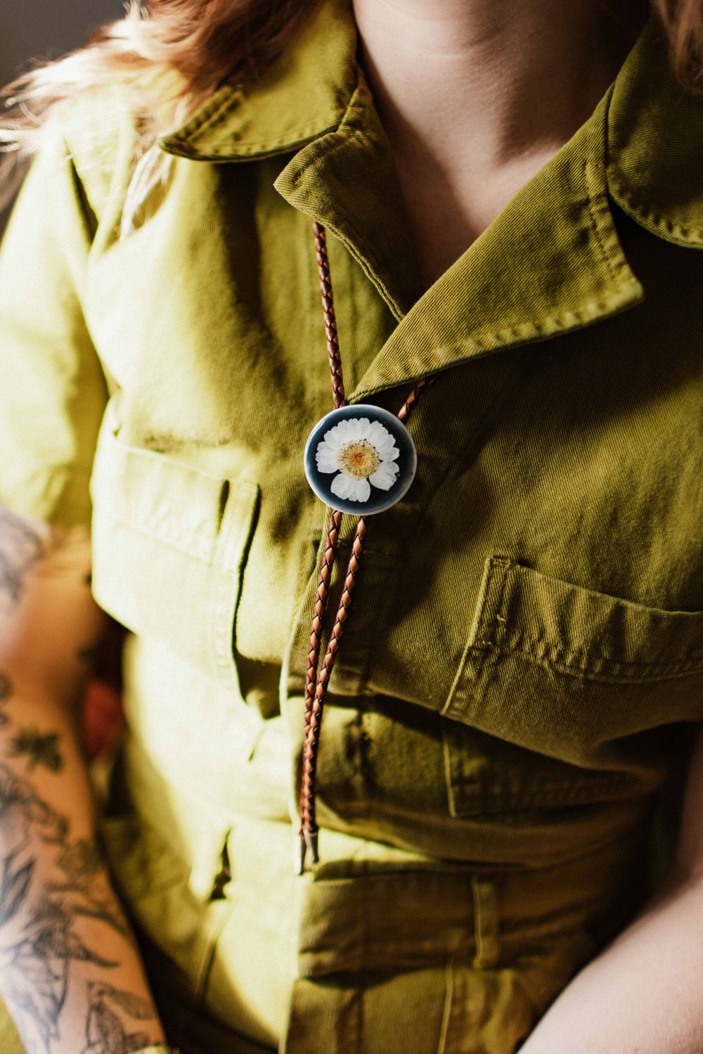 Close-up of handmade pressed flower bolo tie on olive green linen jacket.