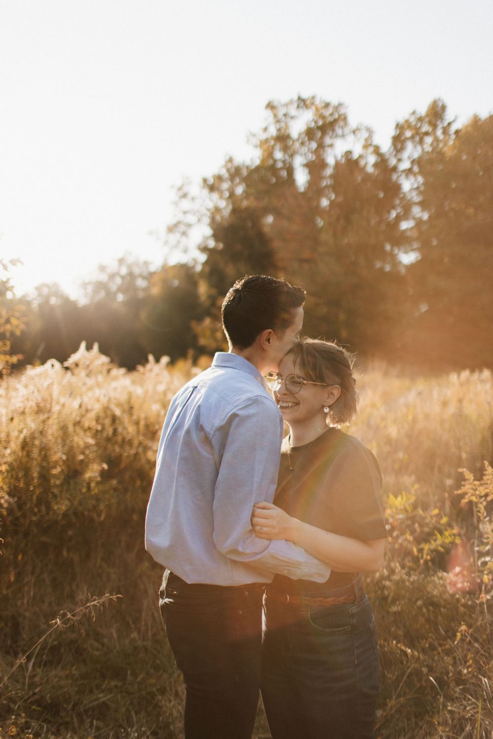 Couple sharing a tender moment in a sunlit autumn field with golden foliage.
