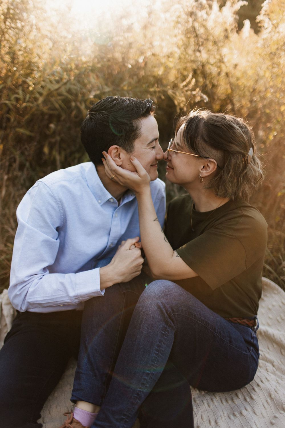 Couple sharing an intimate almost-kiss while sitting outdoors in warm golden sunlight.