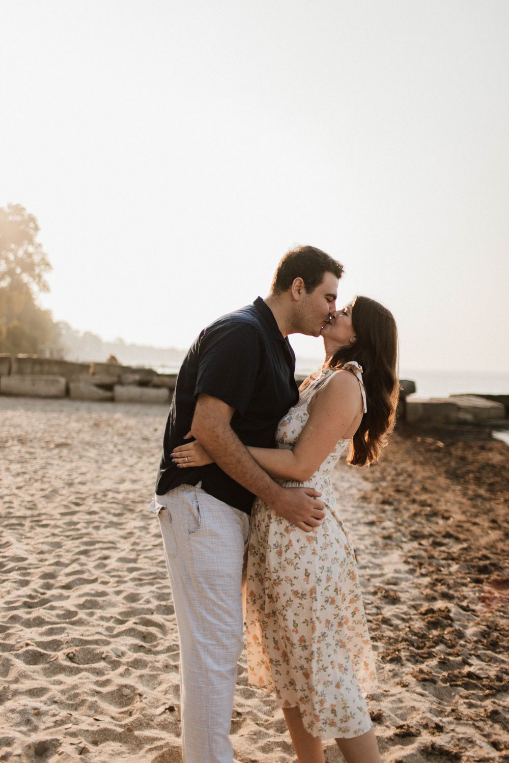Couple sharing a passionate kiss on a sandy beach during golden hour sunset.