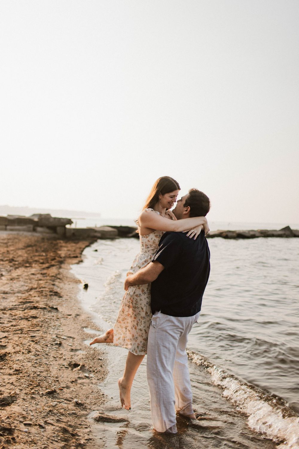 Romantic couple embracing and nearly kissing while standing in shallow beach water.