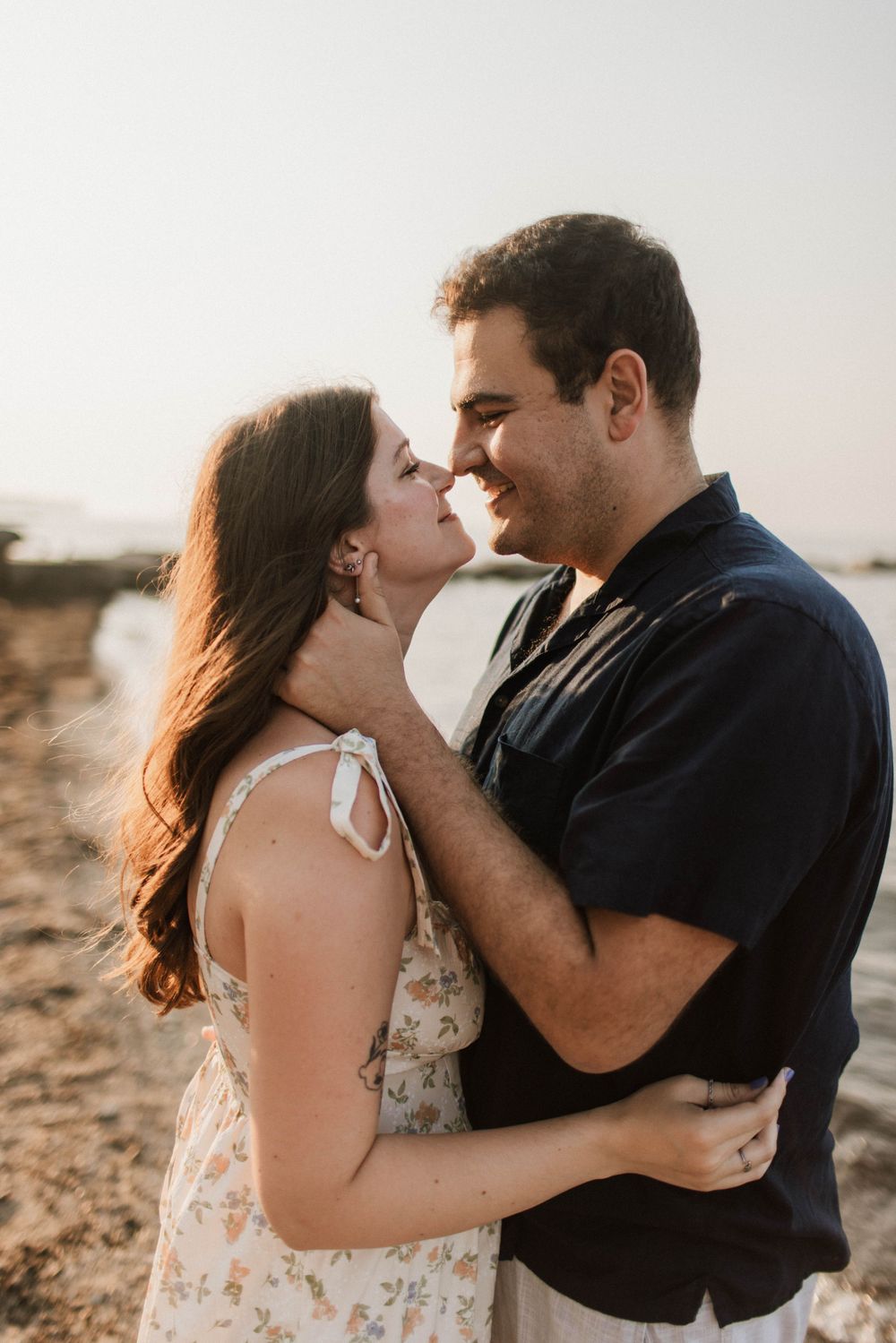 Smiling couple embracing nose-to-nose on a sunlit beach during golden hour.